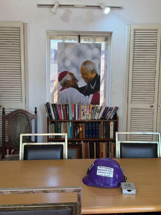 The study in the Tutu family home in Soweto: a portrait of Archbishop Desmond Tutu and Nelson Mandela above a bookcase, and a purple hard hat bearing the Archbishop's name on the table.