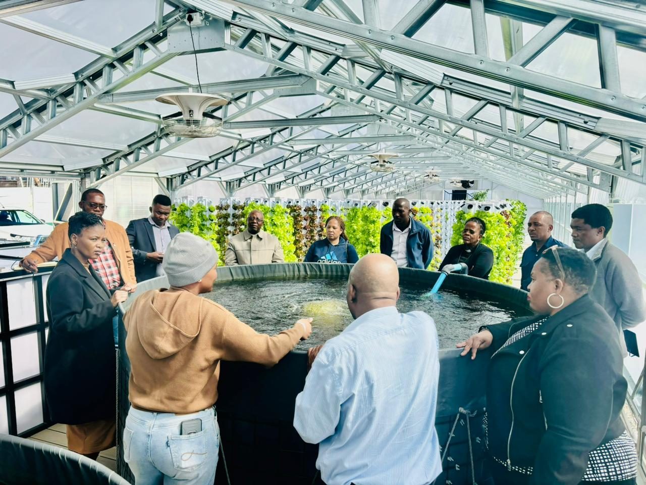 Trainees gather around a fish tank at the Randburg training facility, one with a hand in the water, lettuce towers along the far wall.