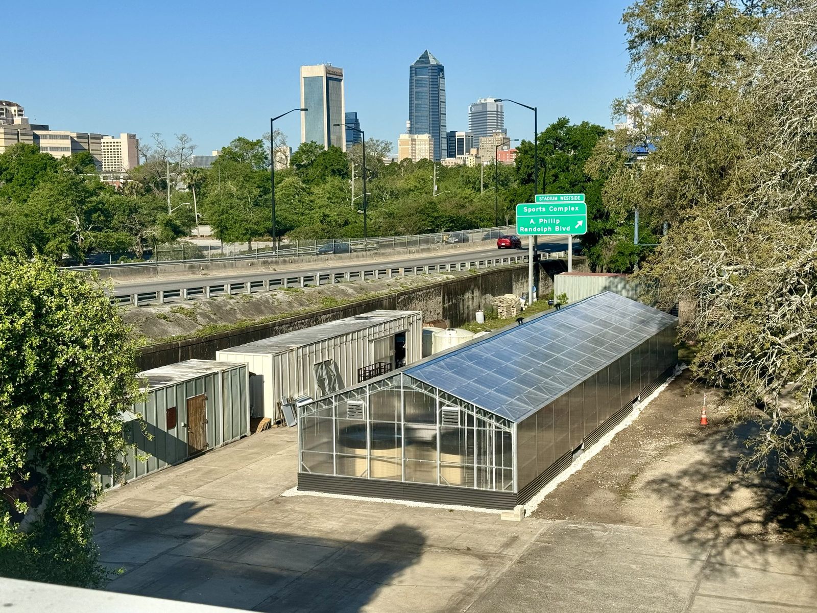 The NativeFresh greenhouse beside its storage containers, with the downtown Jacksonville skyline beyond the expressway.