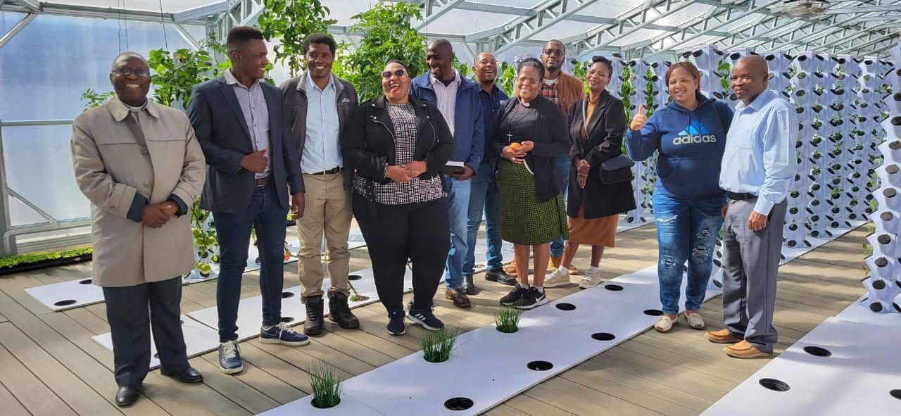 A group of visitors standing together among vertical grow towers inside a FreshMinistries greenhouse.