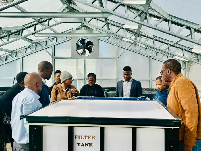 A group gathers round the filter tank of an aquaponics system inside the Randburg greenhouse.